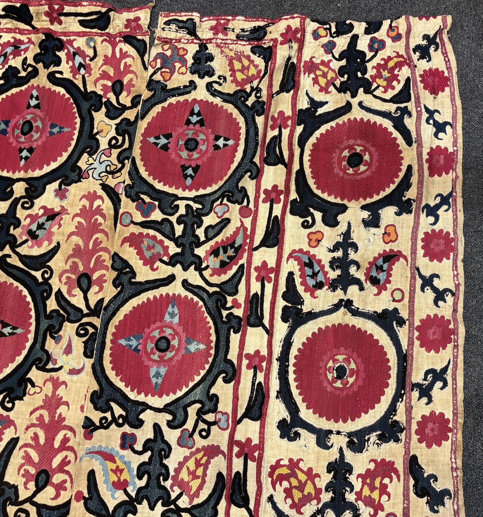 An 19th century Uzbek Suzani embroidered wall hanging, in two pieces, the main hanging sewn together as four panels, together with a fifth matching border, being detached, embroidered with large bold floral motifs, in ri